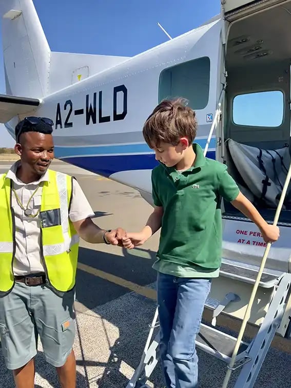 Ein kleiner Junge steigt aus einem Privatjet. Das Flughafenpersonal kümmert sich beim Aussteigen um ihn und hält ihm die Hand.